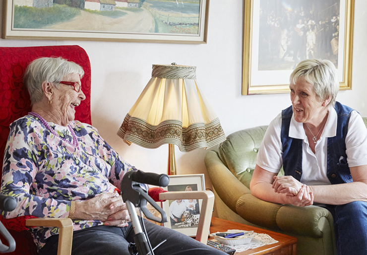 Eldre kvinne hjemme som har besøk av person fra omsorgstjenesten